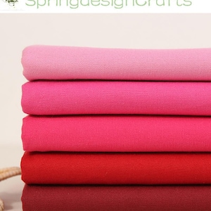 May include: A stack of five folded fabric pieces in a gradient of red and pink shades. The top layer is light pink, followed by medium pink, dark pink, bright red, and a deep burgundy at the bottom. Each piece has a visible woven texture.