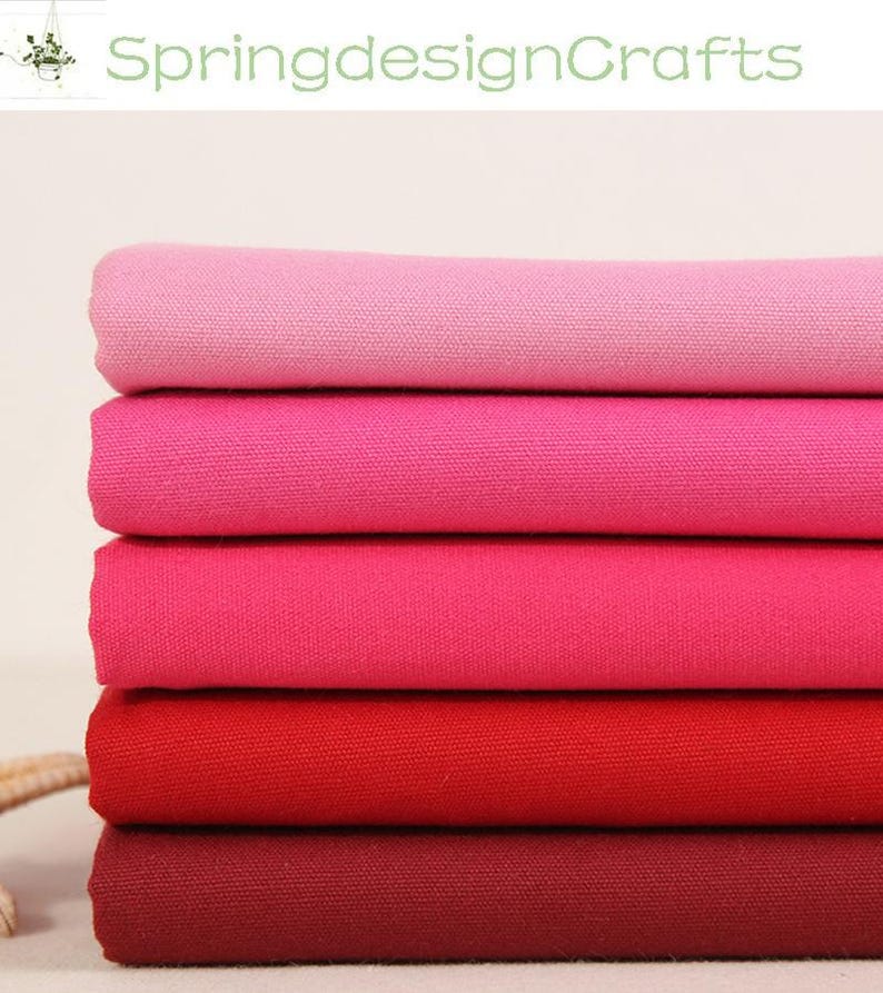 May include: A stack of five folded fabric pieces in a gradient of red and pink shades. The top layer is light pink, followed by medium pink, dark pink, bright red, and a deep burgundy at the bottom. Each piece has a visible woven texture.