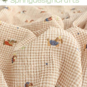 Può includere: Un tessuto con motivo a quadretti vichy beige e bianco caratterizzato da una stampa ripetuta di piccoli cani marroni che indossano vestiti colorati e minuscole stelle blu. Il tessuto ha un aspetto testurizzato e stropicciato con il testo SpringdesignCrafts.