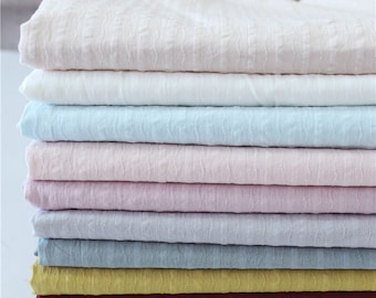 May include: A stack of 10 different colored fabric swatches. The fabrics are all textured and have a subtle sheen. The colors are: white, light blue, pink, light gray, dark gray, yellow, red, and dark blue.