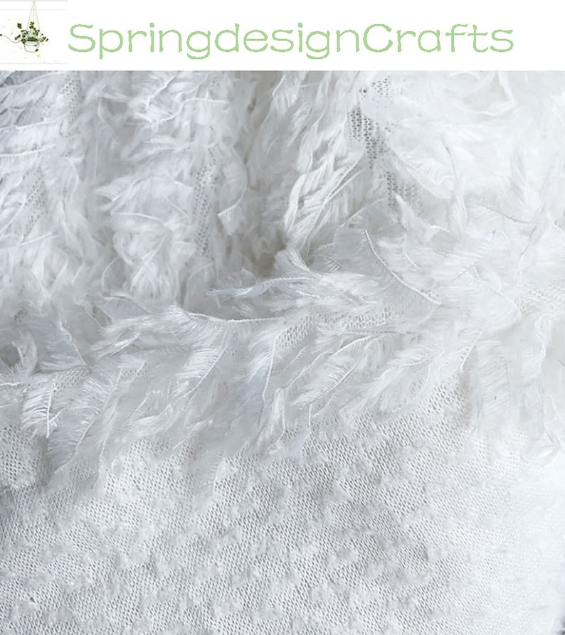 May include: White feather trim fabric with a delicate, lacy texture. The fabric is soft and airy, perfect for adding a touch of elegance to any project.