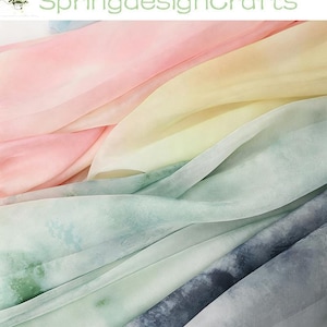 May include: A collection of layered, semi-sheer fabric pieces featuring a soft, watercolor-inspired tie-dye pattern. The colors transition from pale pink and light yellow to muted sage green and a deep, stormy blue, creating a flowing, rippled effect.