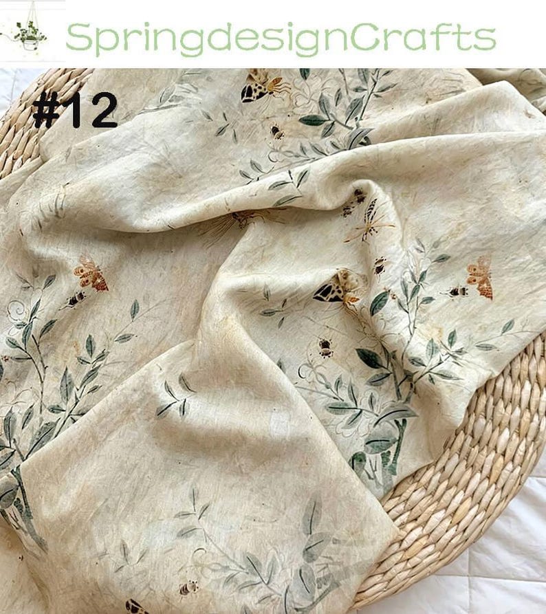 Peut inclure: Tissu cr&egrave;me avec un imprim&eacute; botanique repr&eacute;sentant des papillons, des feuilles et de petits insectes. Le tissu est drap&eacute; sur un panier en osier. Les textes "SpringdesignCrafts" et "#12" sont visibles.