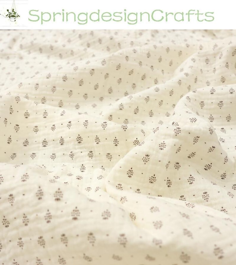 May include: Cream-colored fabric with a repeating pattern of small, dark brown floral or leaf-like shapes. The fabric is soft and textured, with visible folds and wrinkles. The text "SpringdesignCrafts" is in green at the top.