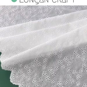 May include: White cotton fabric with a delicate eyelet pattern of small flowers. The fabric has a scalloped edge.