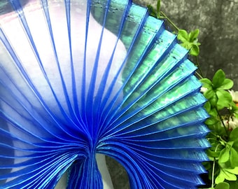 May include: A blue iridescent pleated fabric with a fan-like shape. The fabric is folded and curved, creating a unique and decorative design.