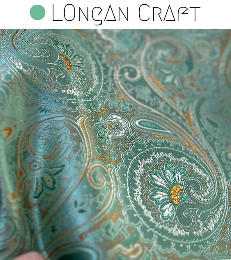 May include: Close-up of a teal paisley fabric with gold and white accents. The fabric has a subtle shimmer and a luxurious feel.