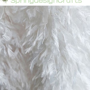 May include: White feather trim fabric with a soft, fluffy texture. The fabric is delicate and airy, perfect for adding a touch of elegance to any project.