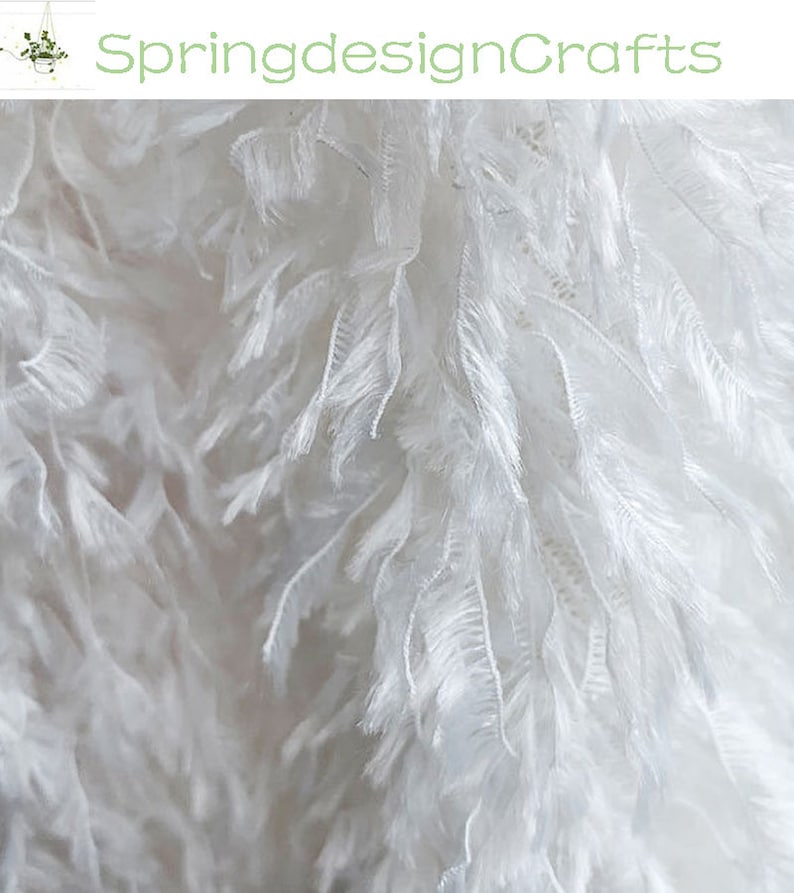 May include: White feather trim fabric with a soft, fluffy texture. The fabric is delicate and airy, perfect for adding a touch of elegance to any project.