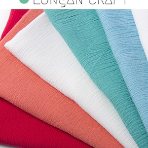 Op de afbeelding: Een waaier van kleurrijke stofstalen in rood, koraal, wit, turquoise en lichtblauw. De stof heeft een getextureerde, gekreukelde uitstraling. De tekst "LONGAN CRAFT" wordt bovenaan weergegeven.