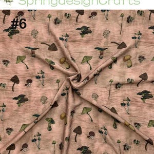 Peut inclure: Un tissu &agrave; motifs r&eacute;p&eacute;t&eacute;s de divers champignons dans des tons de marron, vert et jaune sur un fond beige ros&eacute;. Le tissu est pli&eacute;, montrant la texture et le num&eacute;ro "#6" en noir.