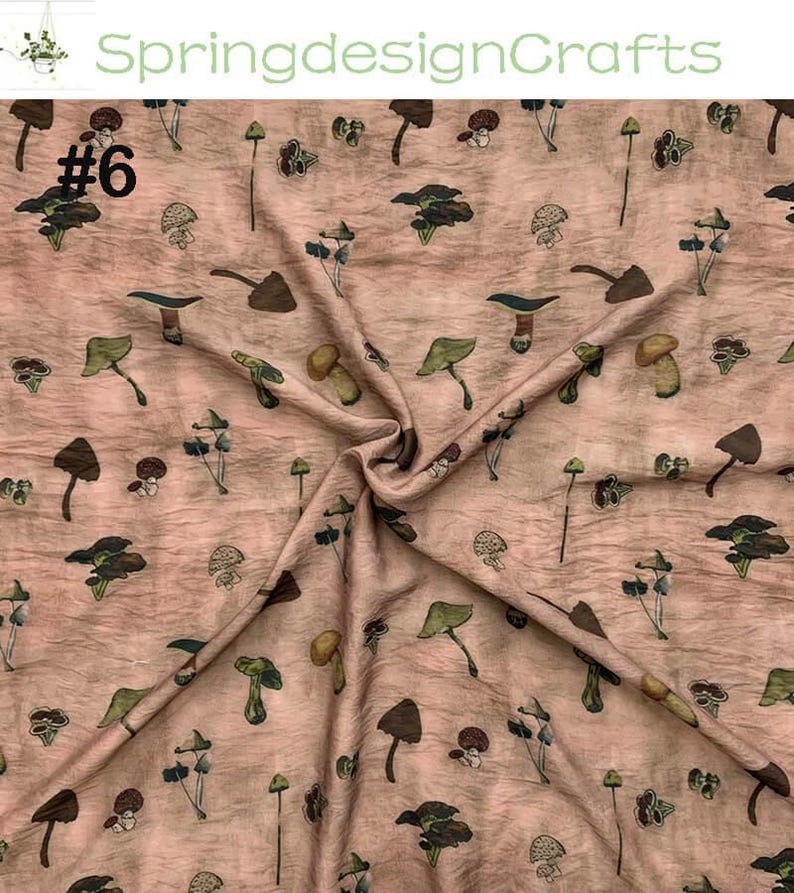 Peut inclure: Un tissu &agrave; motifs r&eacute;p&eacute;t&eacute;s de divers champignons dans des tons de marron, vert et jaune sur un fond beige ros&eacute;. Le tissu est pli&eacute;, montrant la texture et le num&eacute;ro "#6" en noir.