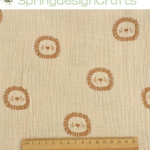 May include: Cream-colored fabric with a repeating pattern of cartoon lion faces in brown. A wooden ruler with inch markings is at the bottom. The text "SpringdesignCrafts" is at the top. The fabric appears to be muslin.