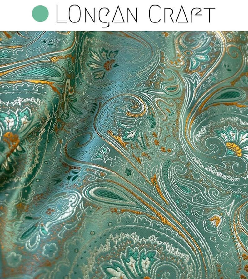 May include: Teal fabric with a gold paisley pattern. The fabric has a subtle sheen and a textured surface.