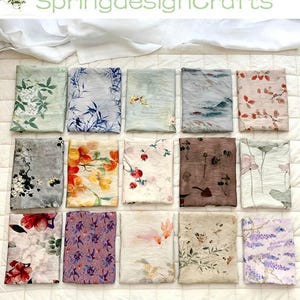 Peut inclure: Une collection d'&eacute;charpes pli&eacute;es avec des motifs floraux et inspir&eacute;s de la nature. Les &eacute;charpes pr&eacute;sentent diverses couleurs, dont le vert, le bleu, le rouge et le violet, avec des motifs d&eacute;taill&eacute;s de fleurs, de feuilles et de paysages. Le texte "SpringdesignCrafts" est visible en haut.