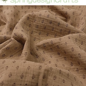 May include: Close-up of a tan fabric with a repeating pattern of small, dark brown floral shapes. The fabric is textured and appears to be soft and flowing. The words "SpringdesignCrafts" are in green text in the upper left corner.
