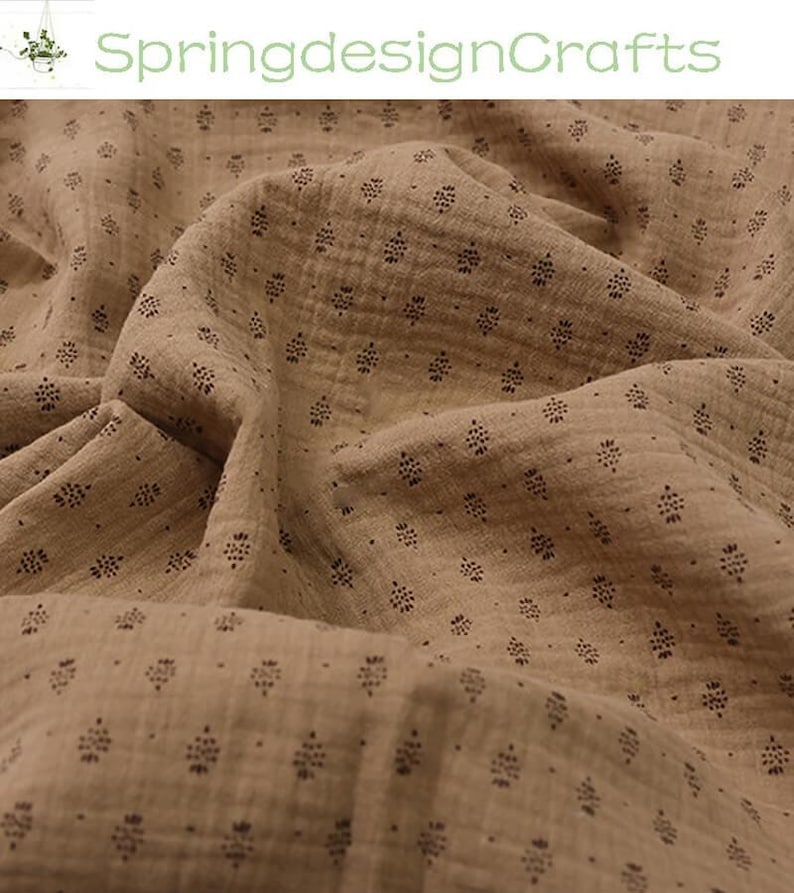 May include: Close-up of a tan fabric with a repeating pattern of small, dark brown floral shapes. The fabric is textured and appears to be soft and flowing. The words "SpringdesignCrafts" are in green text in the upper left corner.