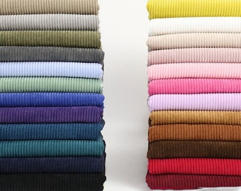 May include: A stack of 14 different colored corduroy fabrics. The fabrics are arranged in a vertical stack, with the lightest color at the top and the darkest color at the bottom. The fabrics are all the same width and length, and they are all folded in half.