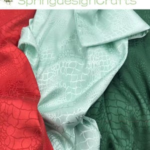 Peut inclure: Gros plan sur du tissu rouge, vert menthe et vert foncé. Le tissu présente un motif texturé ressemblant à de la peau de reptile. Le texte "SpringdesignCrafts" est visible dans le coin supérieur gauche.