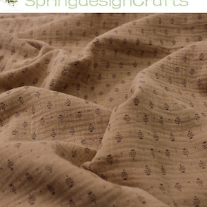 May include: Close-up of tan fabric with a repeating pattern of small, dark floral shapes. The fabric is soft and textured, with visible folds and shadows. The text "SpringdesignCrafts" is in green at the top.