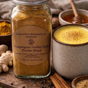 May include: A jar of Adaptogenic Golden Milk Powder Blend, with ingredients including turmeric and ginger, is next to a mug of golden milk. The jar has a label with the text "Hudson River Homeopathy & Apothecary". Cinnamon sticks and honey are also visible.