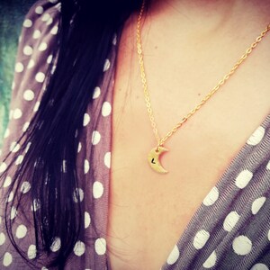 Puede incluir: Un collar de cadena dorada con un colgante de media luna. El colgante tiene una peque&ntilde;a letra "L" grabada. El collar lo lleva una persona con el pelo largo y oscuro y una camisa de lunares.