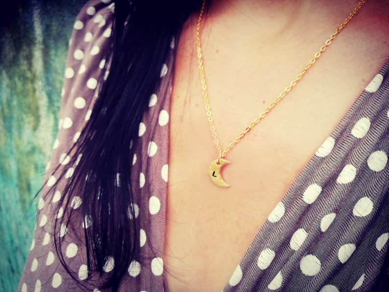 Puede incluir: Un collar de cadena dorada con un colgante de media luna. El colgante tiene una peque&ntilde;a letra "L" grabada. El collar lo lleva una persona con el pelo largo y oscuro y una camisa de lunares.