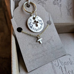 May include: A gold-toned keychain with a round charm featuring a cross and the name "Harlee" engraved on it. A matching gold chain with a small cross pendant is also included.