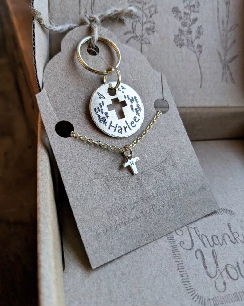 May include: A gold-toned keychain with a round charm featuring a cross and the name "Harlee" engraved on it. A matching gold chain with a small cross pendant is also included.