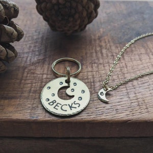 Puede incluir: Un llavero dorado con una etiqueta redonda que presenta un dise&ntilde;o de luna creciente y el nombre "Becks" grabado. Un collar dorado a juego con un colgante de luna creciente m&aacute;s peque&ntilde;o.