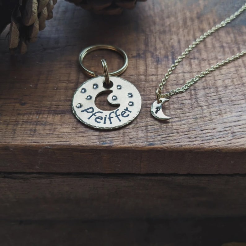 Puede incluir: Un llavero de metal dorado con un dise&ntilde;o de media luna y el nombre "Pfeiffer" grabado en &eacute;l. Tambi&eacute;n se muestra un collar de metal dorado a juego con un colgante de media luna.