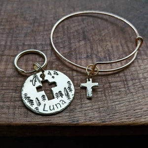 May include: A gold charm bracelet with a cross charm and a gold key chain with a round charm featuring a cross, trees, and the name "Luna".