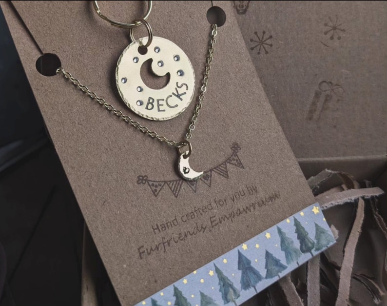 Puede incluir: Un conjunto de collar y llavero de oro con un dije de media luna y el nombre "Becks" grabado en una etiqueta redonda. El conjunto est&aacute; empaquetado en una tarjeta marr&oacute;n con el texto "Hand crafted for you by Furfriends Emporium".