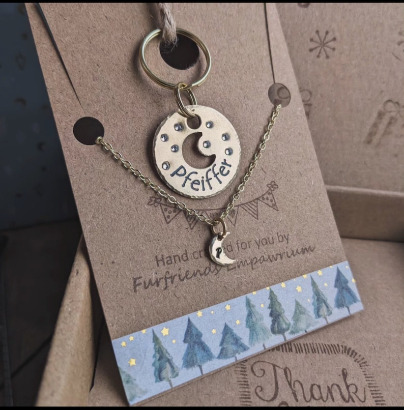 Puede incluir: Conjunto de collar y llavero de oro con un dije de media luna y la palabra "Pfeiffer" grabada en una etiqueta redonda. El conjunto se muestra en una tarjeta marr&oacute;n con una escena de bosque y el texto "Hecho a mano para ti por Furfriends Emporium".