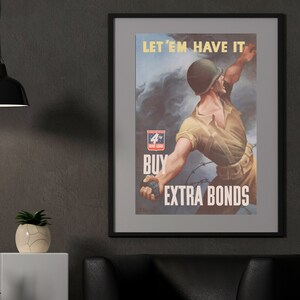 May include: A black leather armchair with a gray rug in front of it. A framed poster with the text "Let 'em have it. Buy extra bonds" hangs on a gray wall. A black lamp hangs from the ceiling above a white pedestal with a potted plant.