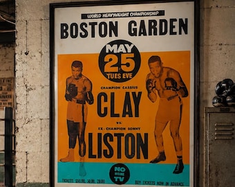 May include: A framed vintage boxing poster for the World Heavyweight Championship at Boston Garden featuring Cassius Clay versus Sonny Liston on May 25. The poster has a white background with orange and blue sections, black text, and illustrations of two boxers.