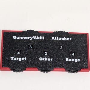 May include: A rectangular game board with a black surface and red trim. The board is divided into three sections labeled "Gunnery/Skill", "Attacker", and "Range". Each section has numbers and text.