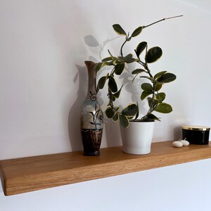Pu&ograve; includere: Uno scaffale in legno con un vaso, una pianta in vaso e un portacandele nero. Lo scaffale &egrave; realizzato in legno naturale e ha un aspetto rustico.