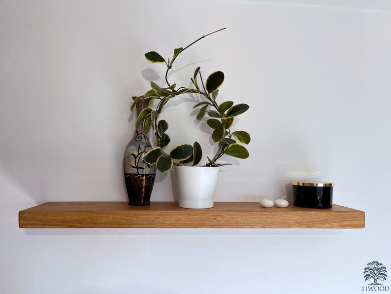 Pu&ograve; includere: Uno scaffale in legno con una pianta in vaso, un vaso decorativo e due candele bianche. Lo scaffale &egrave; montato su una parete bianca.