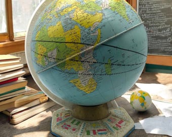 May include: A vintage blue globe with a yellow and green map of the world. The globe is on a base with flags of different countries around the edge. The globe is sitting on a wooden table.