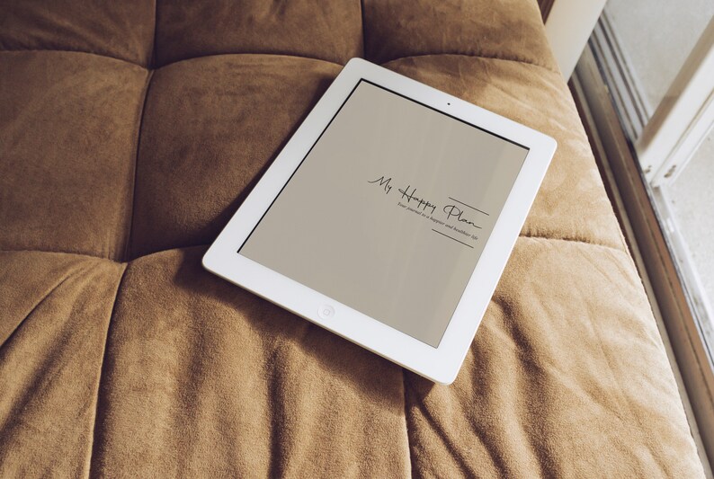 May include: A white tablet computer with a light brown screen displaying the text "My Happy Plan" on a brown couch.