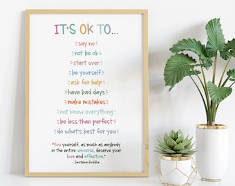 May include: A framed print with the text "It's OK to..." followed by a list of phrases in different colors, including "say no", "not be ok", "start over", "be yourself", "ask for help", "have bad days", "make mistakes", "not know everything", "be less than perfect", and "do what's best for you". The print is on a white shelf with two potted plants.