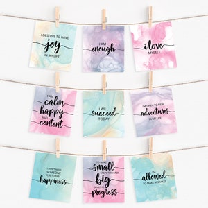 K&ouml;nnte beinhalten: Neun Aquarellkarten mit positiven Affirmationen darauf gedruckt. Die Karten h&auml;ngen an einer Schnur mit W&auml;scheklammern. Die Affirmationen beinhalten "Ich verdiene es, Freude in meinem Leben zu haben", "Ich bin genug", "Ich liebe mich selbst", "Ich bin ruhig, gl&uuml;cklich und zufrieden", "Ich werde heute erfolgreich sein", "Ich bin offen f&uuml;r neue Abenteuer in meinem Leben", "Ich brauche niemanden sonst, um Gl&uuml;ck zu empfinden", "Kleine Schritte in Richtung gro&szlig;er Ziele sind Fortschritt", und "Ich darf Fehler machen".