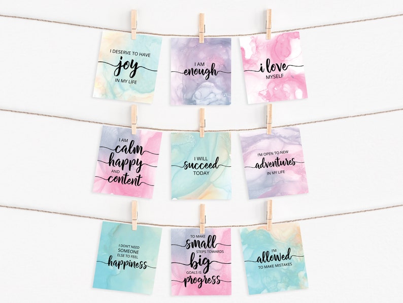 K&ouml;nnte beinhalten: Neun Aquarellkarten mit positiven Affirmationen darauf gedruckt. Die Karten h&auml;ngen an einer Schnur mit W&auml;scheklammern. Die Affirmationen beinhalten "Ich verdiene es, Freude in meinem Leben zu haben", "Ich bin genug", "Ich liebe mich selbst", "Ich bin ruhig, gl&uuml;cklich und zufrieden", "Ich werde heute erfolgreich sein", "Ich bin offen f&uuml;r neue Abenteuer in meinem Leben", "Ich brauche niemanden sonst, um Gl&uuml;ck zu empfinden", "Kleine Schritte in Richtung gro&szlig;er Ziele sind Fortschritt", und "Ich darf Fehler machen".