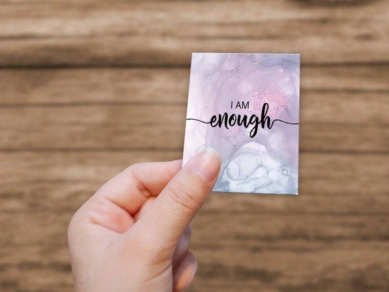 K&ouml;nnte beinhalten: Eine wei&szlig;e Karte mit einem rosa und grauen Aquarellhintergrund. Die Karte tr&auml;gt den Text "I AM enough" in schwarzer Kursivschrift.