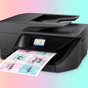 K&ouml;nnte beinhalten: Ein schwarzer All-in-One-Drucker mit einem farbigen Touchscreen-Display. Der Drucker druckt ein Blatt Papier mit bunten Aquarelldesigns und den Worten "space", "joy", "peace", "allowed" und "heal".