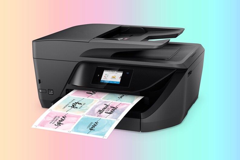 K&ouml;nnte beinhalten: Ein schwarzer All-in-One-Drucker mit einem farbigen Touchscreen-Display. Der Drucker druckt ein Blatt Papier mit bunten Aquarelldesigns und den Worten "space", "joy", "peace", "allowed" und "heal".