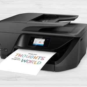 May include: A black all-in-one printer with a color touchscreen display. A sheet of paper with the text "Change your THOUGHTS and you change your WORLD" printed in colorful letters is exiting the printer.