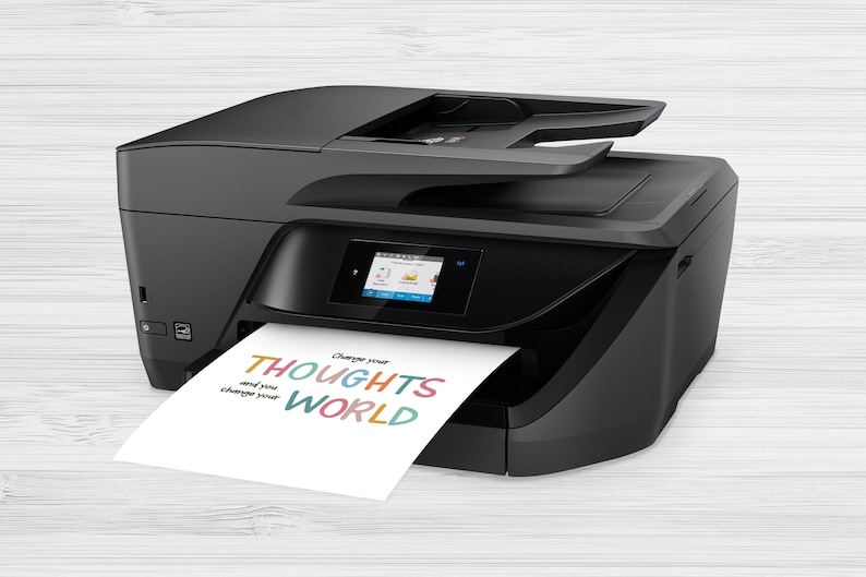 May include: A black all-in-one printer with a color touchscreen display. A sheet of paper with the text "Change your THOUGHTS and you change your WORLD" printed in colorful letters is exiting the printer.