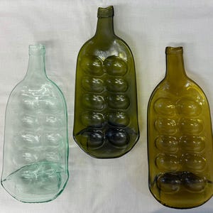 May include: Three glass bottle serving dishes, two are green and one is clear. The dishes have indentations for holding snacks or appetizers.